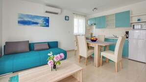 Ein modernes Wohnzimmer mit einem türkisfarbenen Sofa, einem Esstisch mit Stühlen, einer Küchenzeile mit türkisfarbenen Schränken und einem kleinen Tisch mit Blumen.