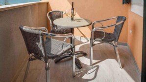 Un balcon avec des fauteuils en osier et une table, une fenêtre donnant sur la mer et un luminaire au plafond.