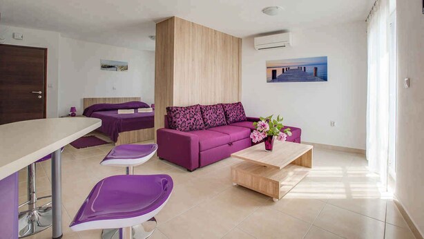 Un salon moderne avec un canapé violet, une table basse en bois et un coin repas comprenant une table blanche et des chaises violettes.