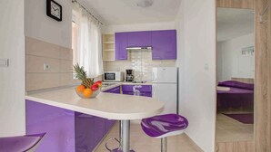 Une cuisine compacte avec des meubles de couleur violette, un four à micro-ondes, une machine à café et un panier de fruits posé sur le comptoir.