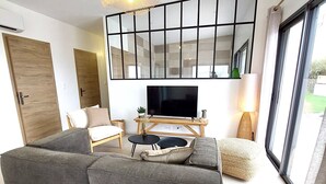 Una sala de estar moderna con un sofá seccional gris, un televisor de pantalla plana, una mesa de centro de madera y un ventanal con vistas al exterior.