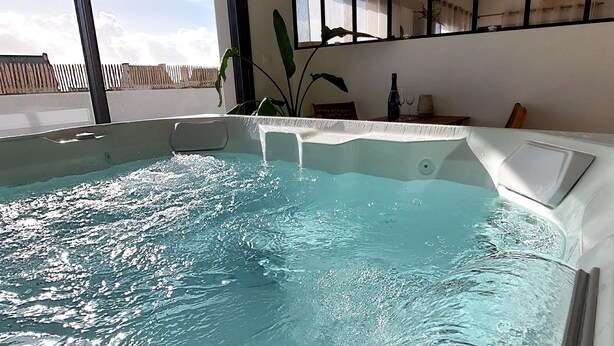 Una piscina interior moderna con agua cristalina, ventanas amplias y un ventilador de techo.