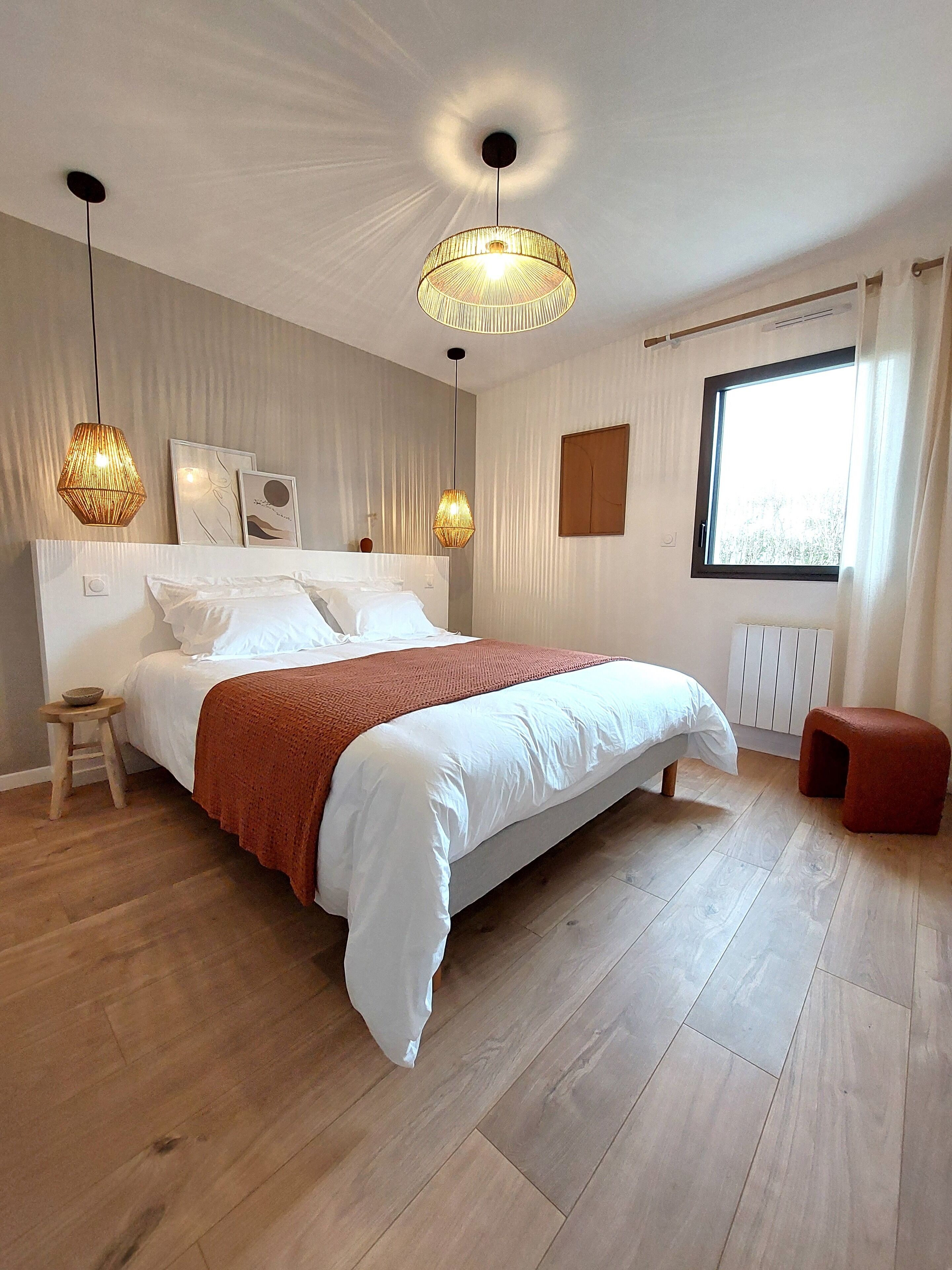 Un dormitorio moderno con una cama grande, dos lámparas de noche, una ventana con cortinas y piso de madera.