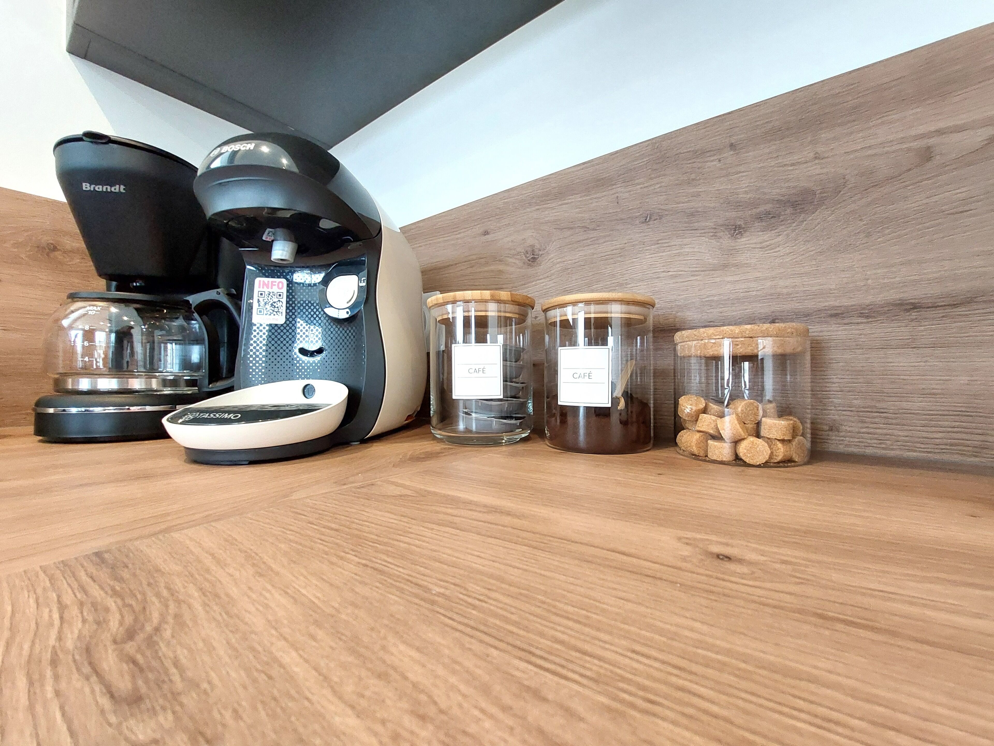 A kitchen counter with a coffee maker, a scale, and three glass jars labeled "CAFÉ".