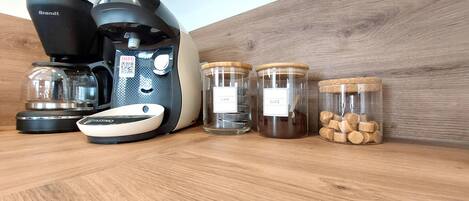 A kitchen counter with a coffee maker, a scale, and three glass jars labeled "CAFÉ".