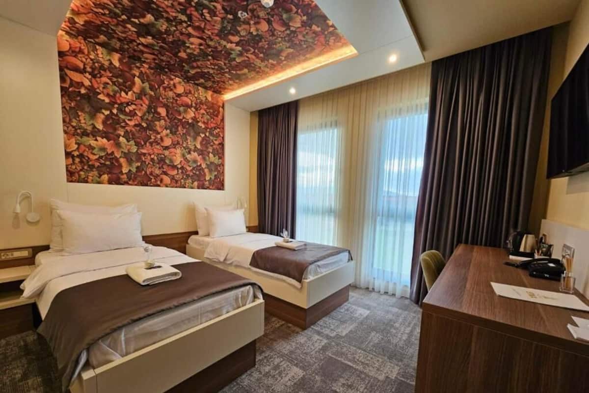 Ein Hotelzimmer mit zwei Betten, einem Schreibtisch und einer Wand mit großem Blumenmuster.
