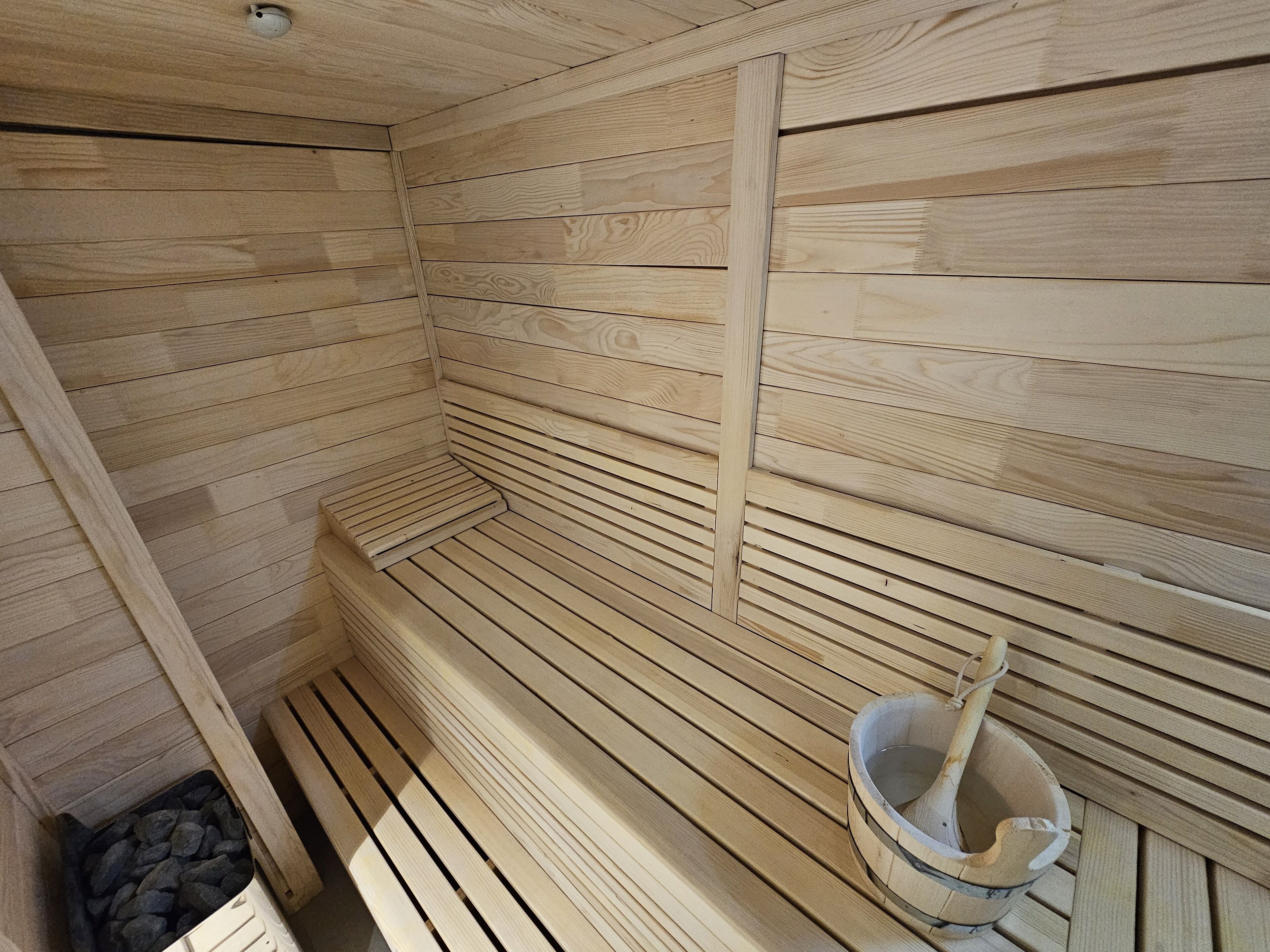 A sauna with wooden walls and benches, a bucket, and a pile of rocks.