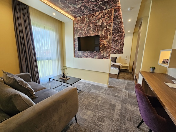 Ein modernes Wohnzimmer mit einer Couch, einem Couchtisch, einem an einer blumengemusterten Wand montierten Fernseher und einem Schreibtisch mit einer Lampe.