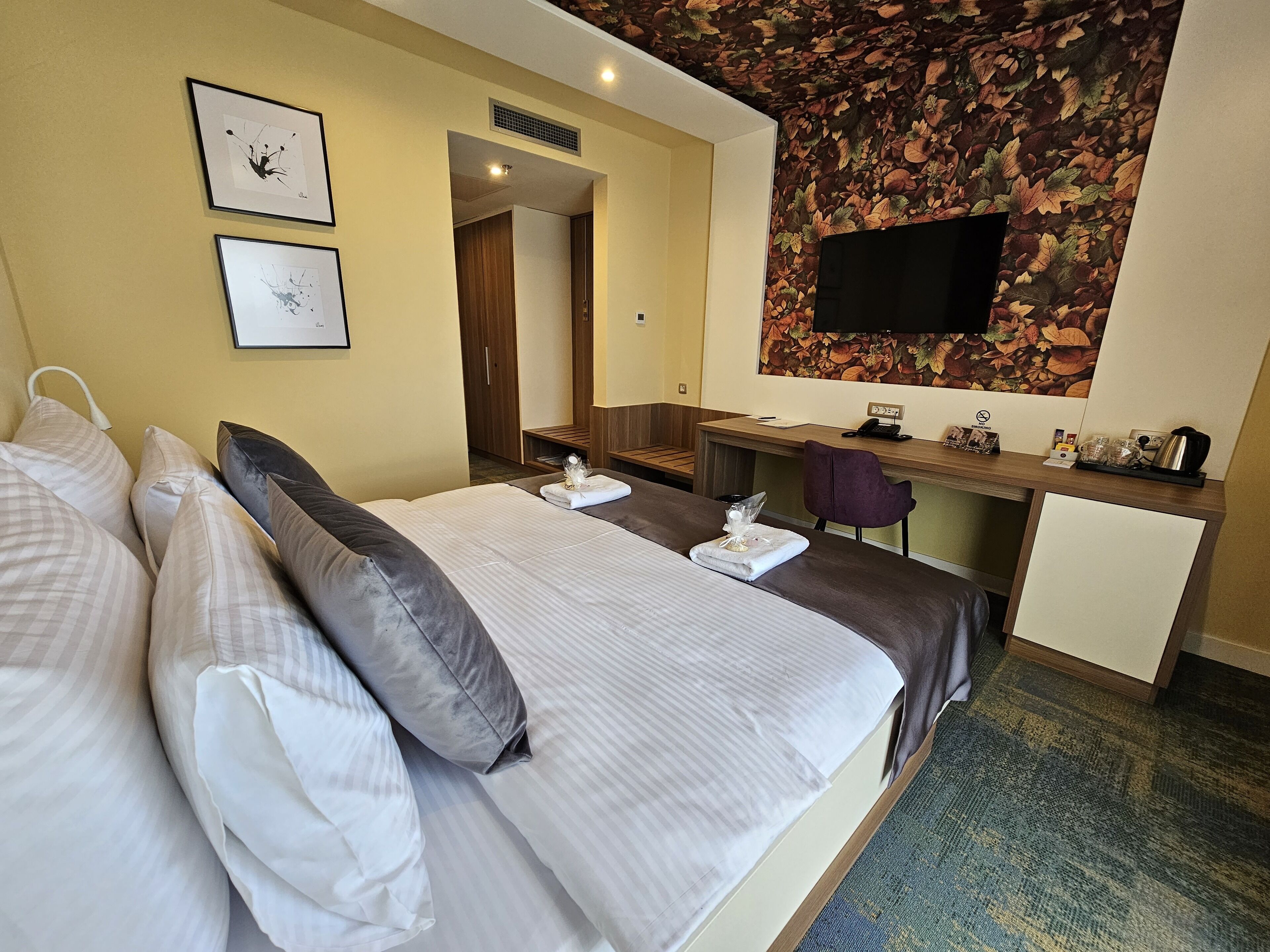 Une chambre d’hôtel avec un lit, un bureau, une chaise, une télévision et une salle de bain visible à travers une porte ouverte.