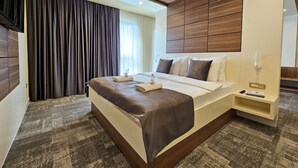 Ein Hotelzimmer mit einem großen Bett, einem Nachttisch mit Lampe, einer Steckdose und einem kleinen Regal mit Fernbedienung und Buch.