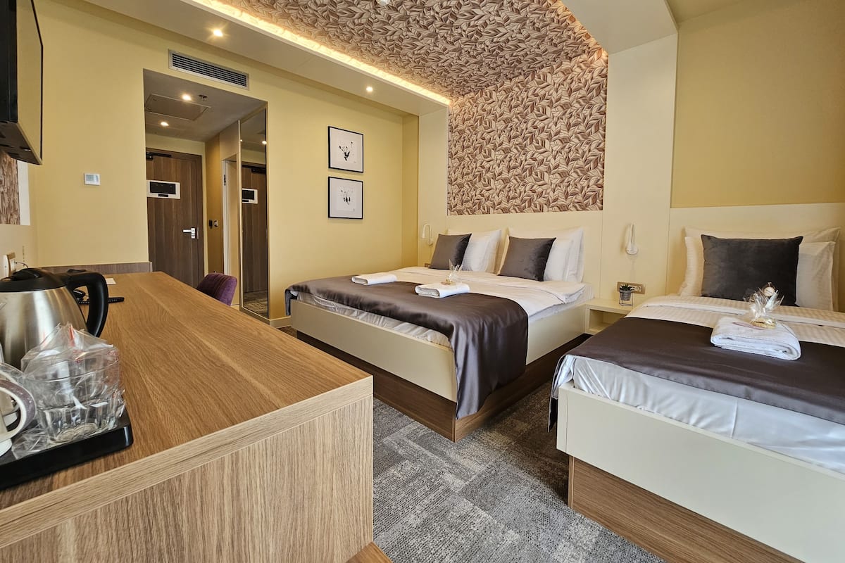 Ein Hotelzimmer mit zwei Betten, einem Holztisch und einer gemusterten Decke.