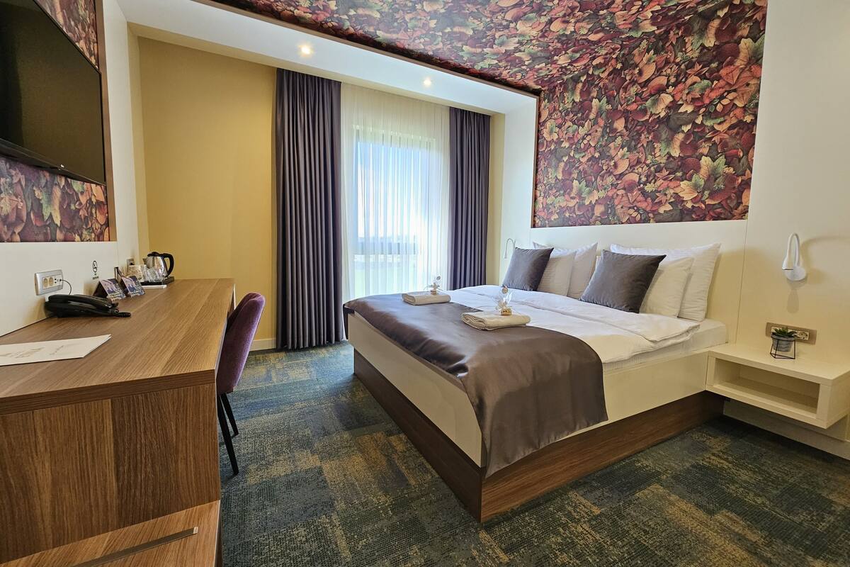 Ein Hotelzimmer mit Bett, Schreibtisch, Stuhl, kleinem Tisch und einem an der Wand befestigten Fernseher.