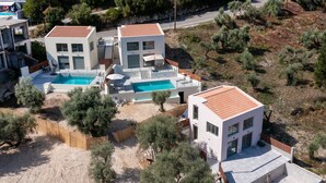 Une maison moderne à deux étages avec une piscine, entourée d’arbres et dotée d’une cour clôturée.