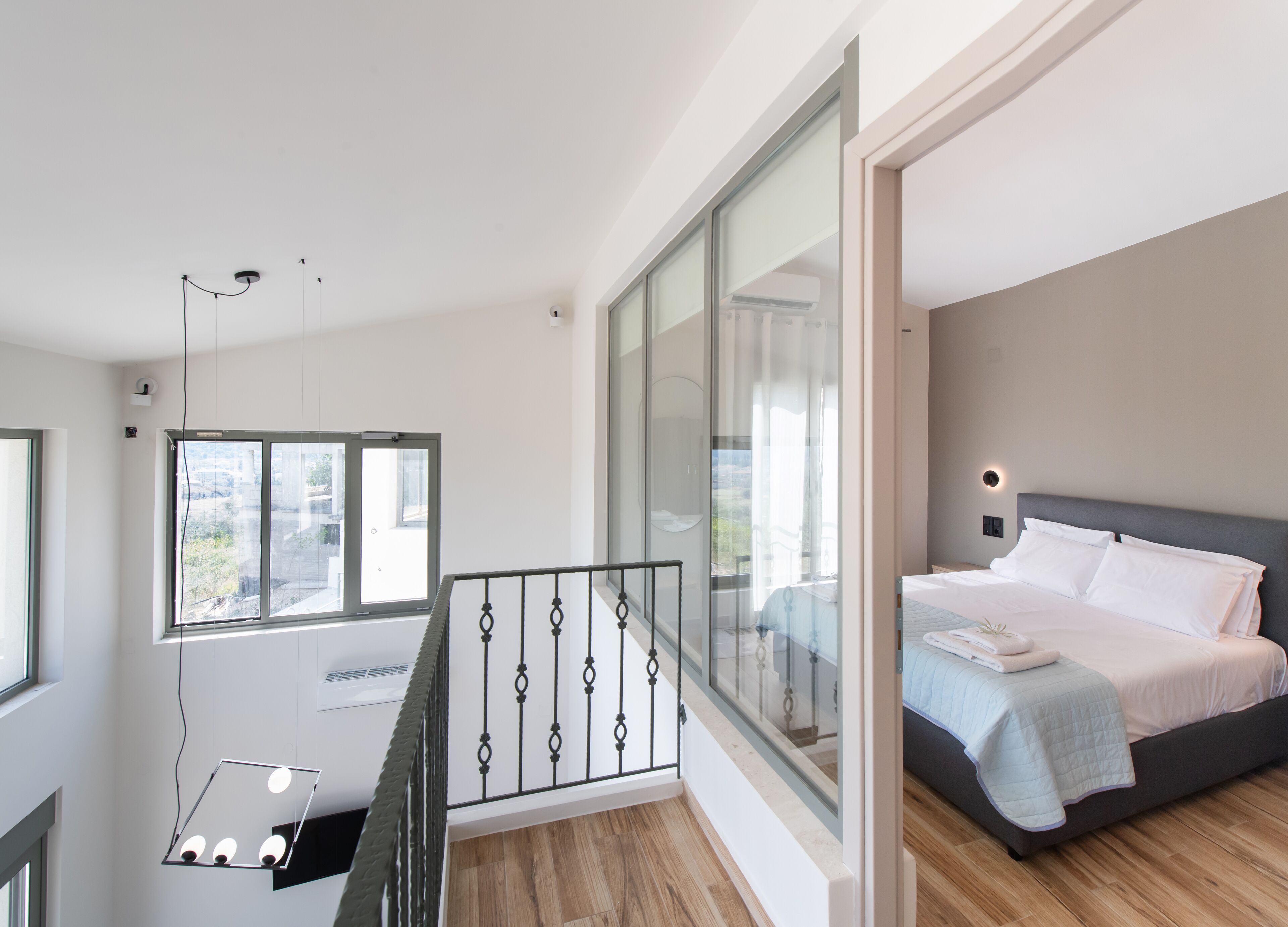 A modern bedroom with a large bed, a balcony with a glass railing, and a view of the city.