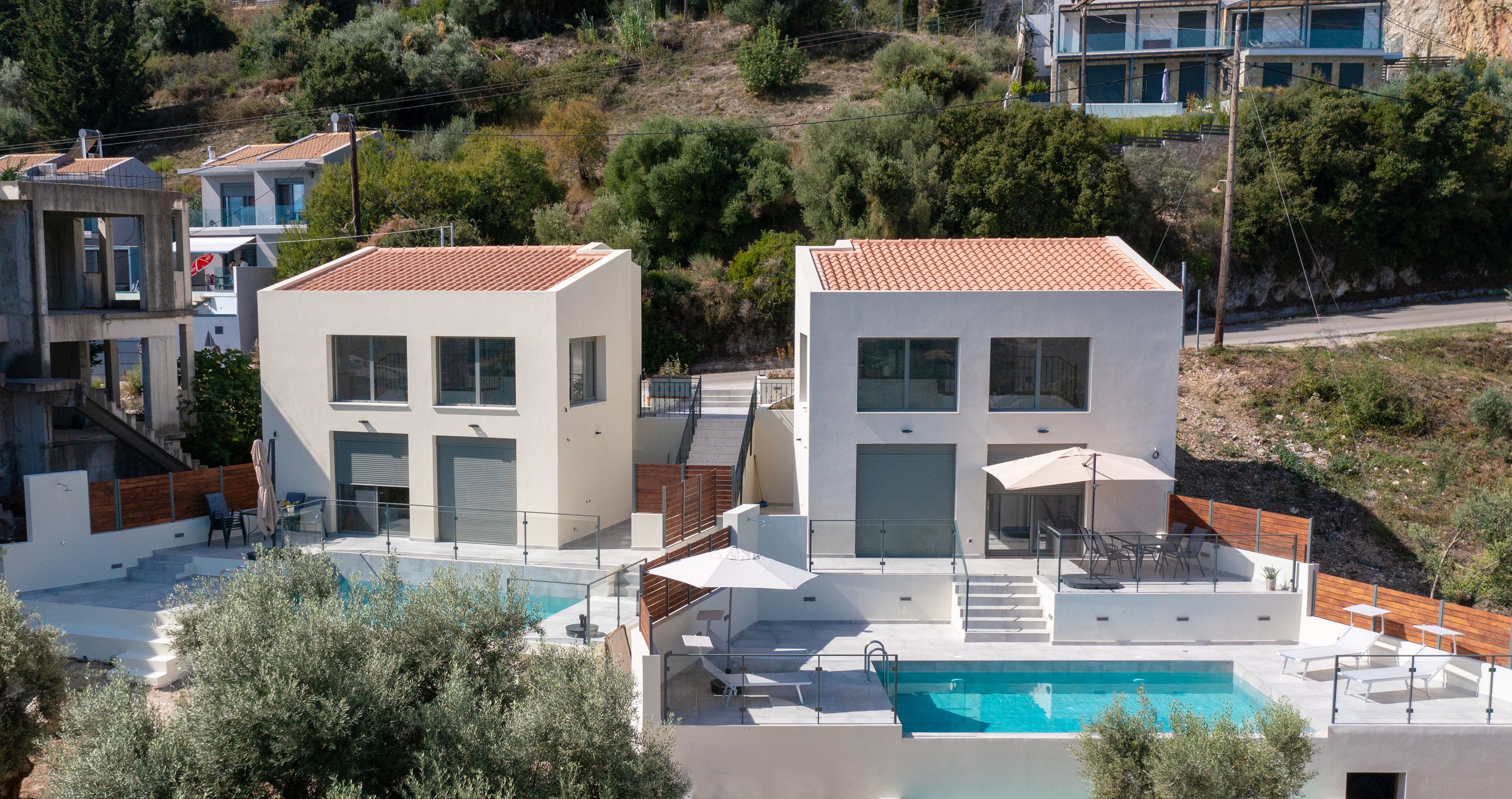 A modern two-story building with a swimming pool, outdoor seating, and a view of surrounding houses.