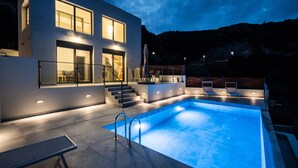 Une maison moderne dotée d’une piscine, d’un espace salon extérieur et d’un escalier menant à l’entrée.