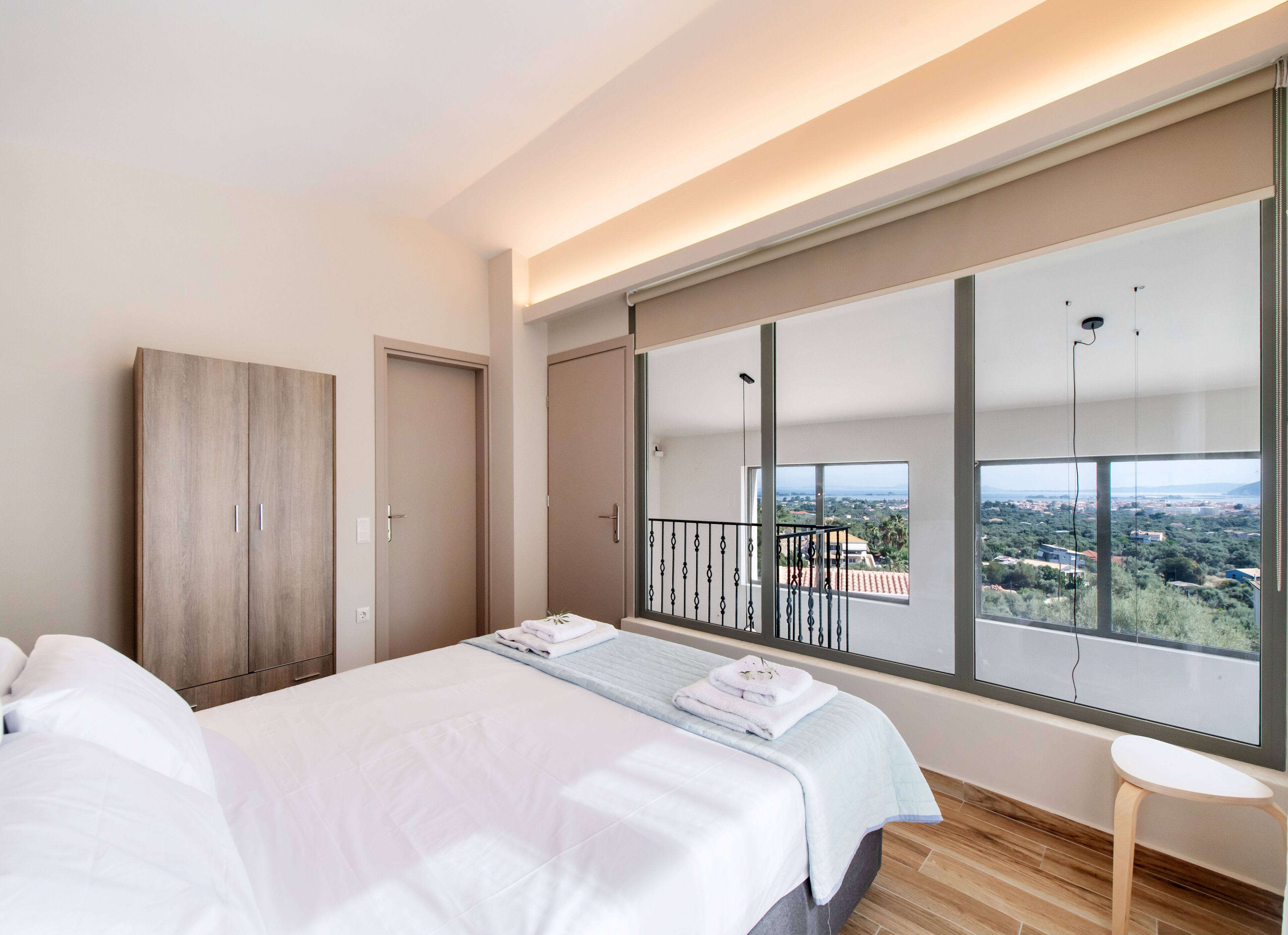 A modern bedroom with a large bed, a wardrobe, and a balcony with a city view.