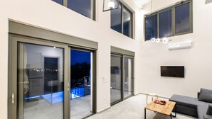 A modern interior with a large sliding glass door leading to a balcony, a flat-screen TV mounted on the wall, and a wooden coffee table. - Elthea Villa 2 in Apolpena, Lefkada (Lefkada)