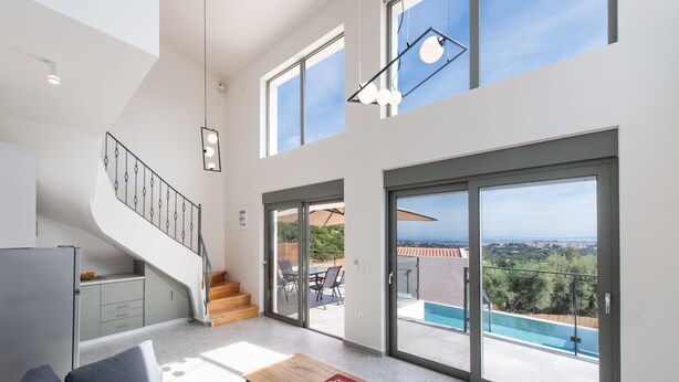 Un vaste espace de vie comprenant un escalier, une table à manger et de grandes portes-fenêtres coulissantes donnant sur une piscine.