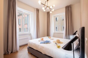 A modern hotel room with a large bed, a bedside table, a lamp, and a view of the city through the windows. - Novos Centro Apartments (Lugano)
