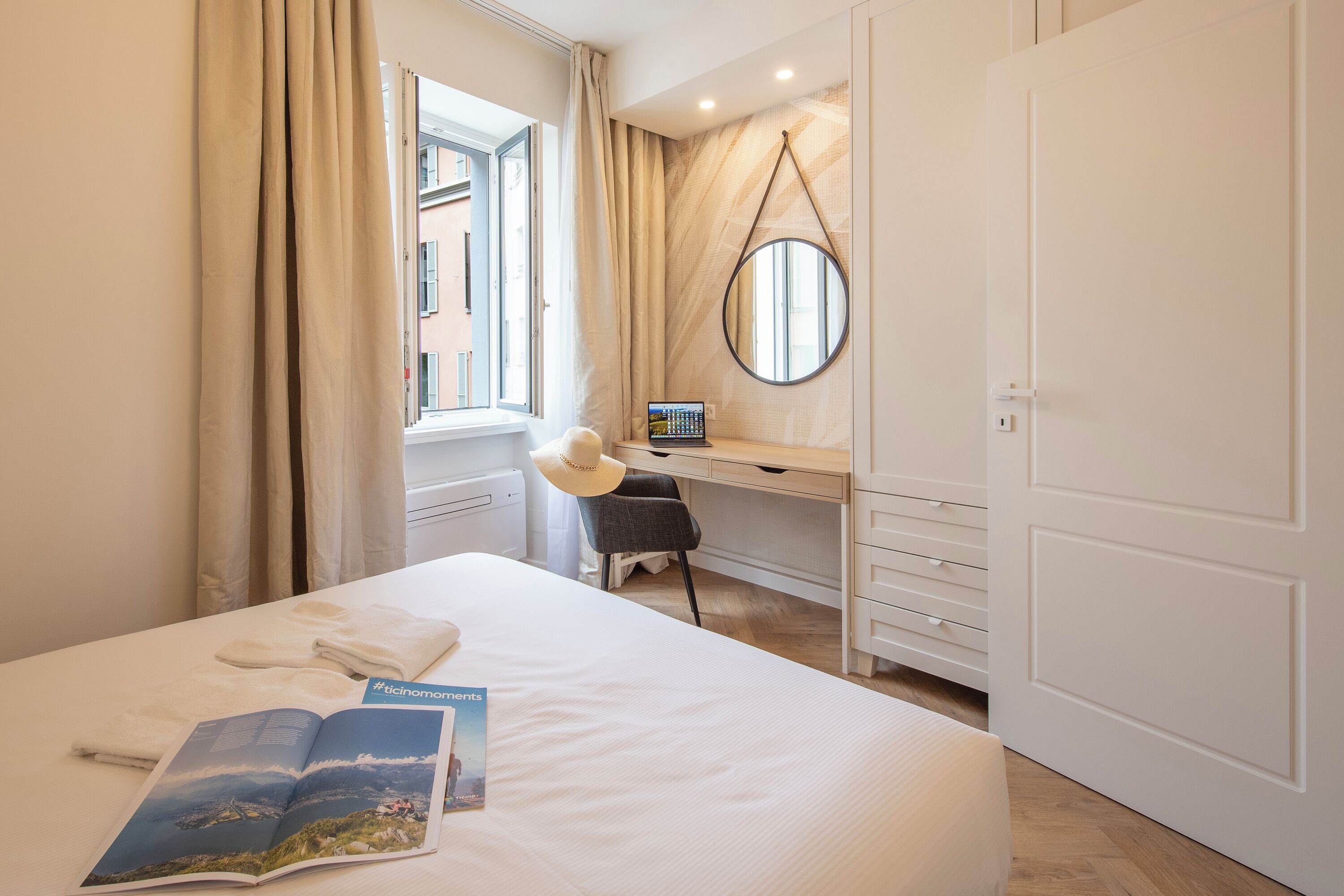 Une chambre d’hôtel avec un lit, un bureau, une chaise, une armoire et une fenêtre avec des rideaux.
