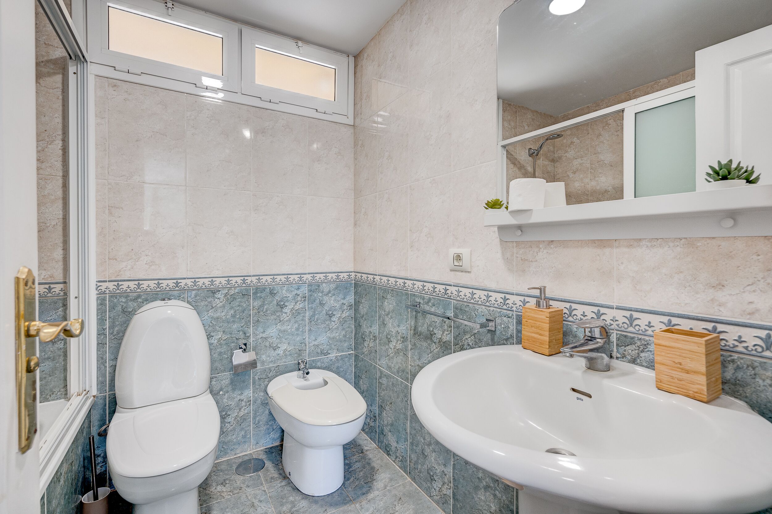 A bathroom with a toilet, bidet, and sink, featuring marble tiles and a small window.