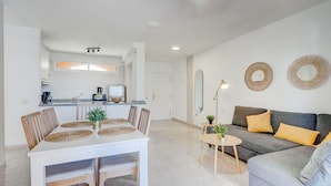 Een moderne woonkamer met een grijze bank, een eettafel met stoelen en een keuken op de achtergrond.