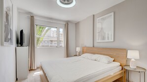 Een moderne slaapkamer met een houten bed, een televisie, een raam met gordijnen en een plafondventilator.