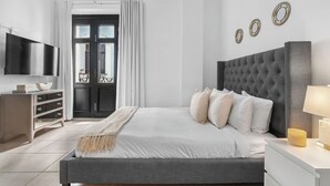 Ein modernes Schlafzimmer mit einem großen Bett, einem Flachbildfernseher, einer Kommode und einem Fenster mit Vorhängen.