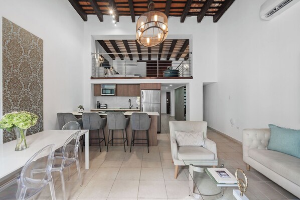 A modern kitchen with a central island, a dining area with clear chairs, and a living room with a sofa and a coffee table.