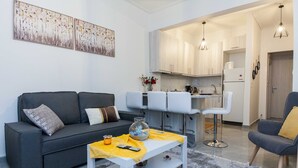 A modern living room with a grey sofa, white coffee table, and a kitchen area with white cabinets and bar stools. - Ano Kipseli Athens Gem 1 Bd Apt for 4 (Athens)