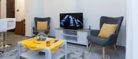 Uma sala de estar moderna com televisão, dois poltronas, uma mesa de centro e um relógio na parede.