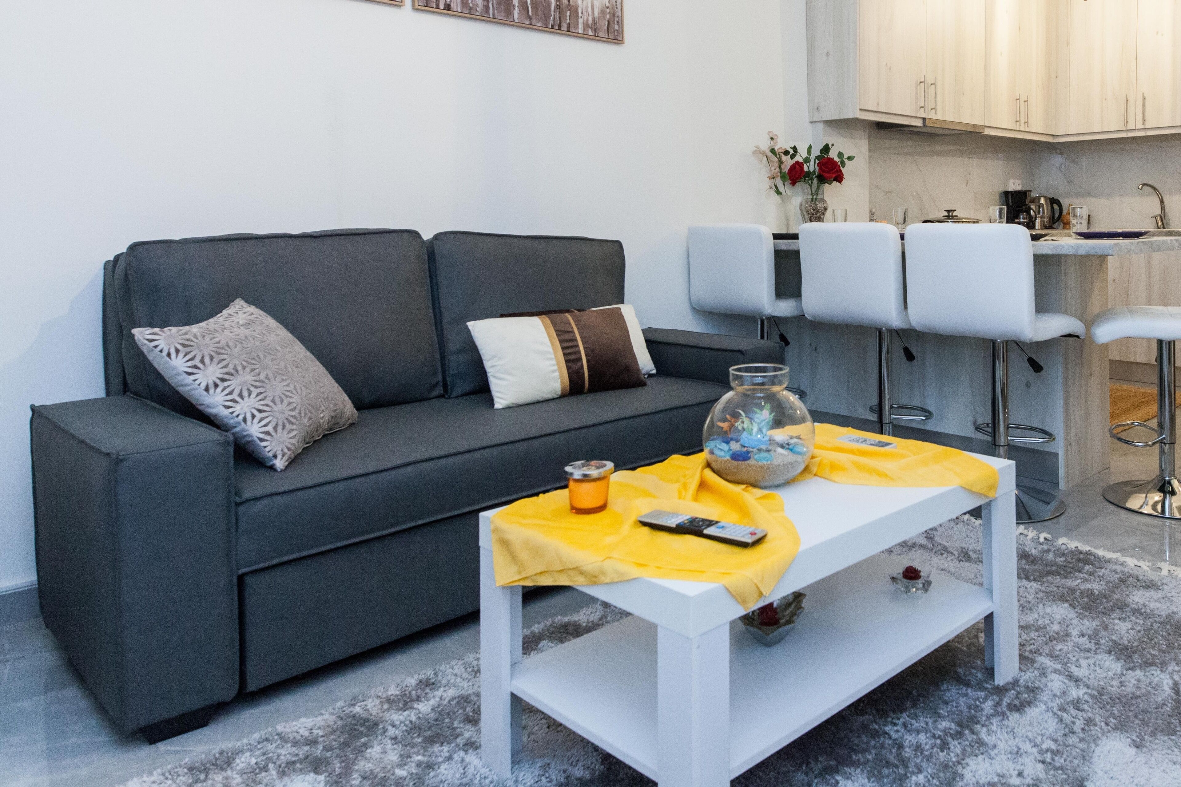 Ein modernes Wohnzimmer mit grauem Sofa, einem weißen Couchtisch und einer Küchenzeile mit Barhocker.