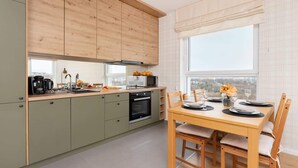 A modern kitchen with wooden cabinets, a dining table set for four, and a large window offering a city view.