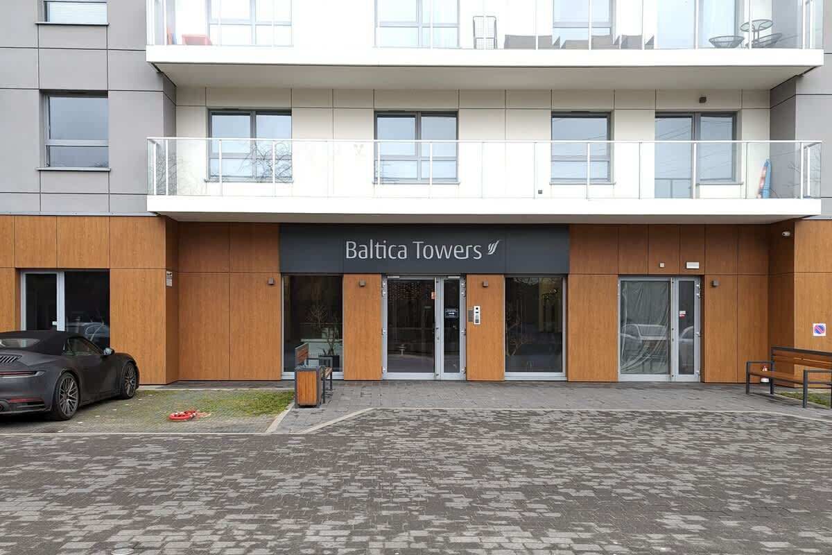 The entrance to the apartment building, featuring a modern design with a wooden facade, glass doors, and neatly paved surroundings.

