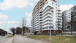 A multi-story residential building with balconies, a parking sign, and a pedestrian pathway.