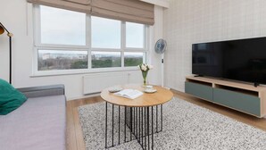 A modern living room with a large window, a round coffee table, a flat-screen TV, and a minimalist design.