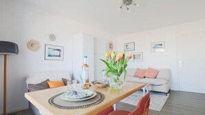 A dining area with a wooden table, red chairs, a vase of tulips, and a white sofa in the background. - Studio Cosy-balcon vue Mer-wifi (Berck)