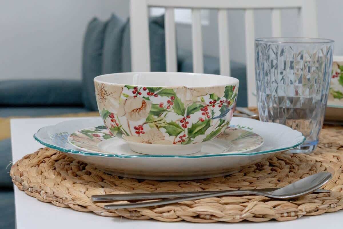 Un tazón con estampado floral sobre un plato blanco, una copa y un posavasos tejido en una mesa.