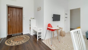 A modern living room with a wooden door, white shelving, a red high chair, a TV mounted on the wall, and a patterned rug.