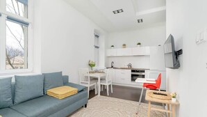 A modern living room with a sofa, a dining table, and a kitchen area with white cabinets and a TV.