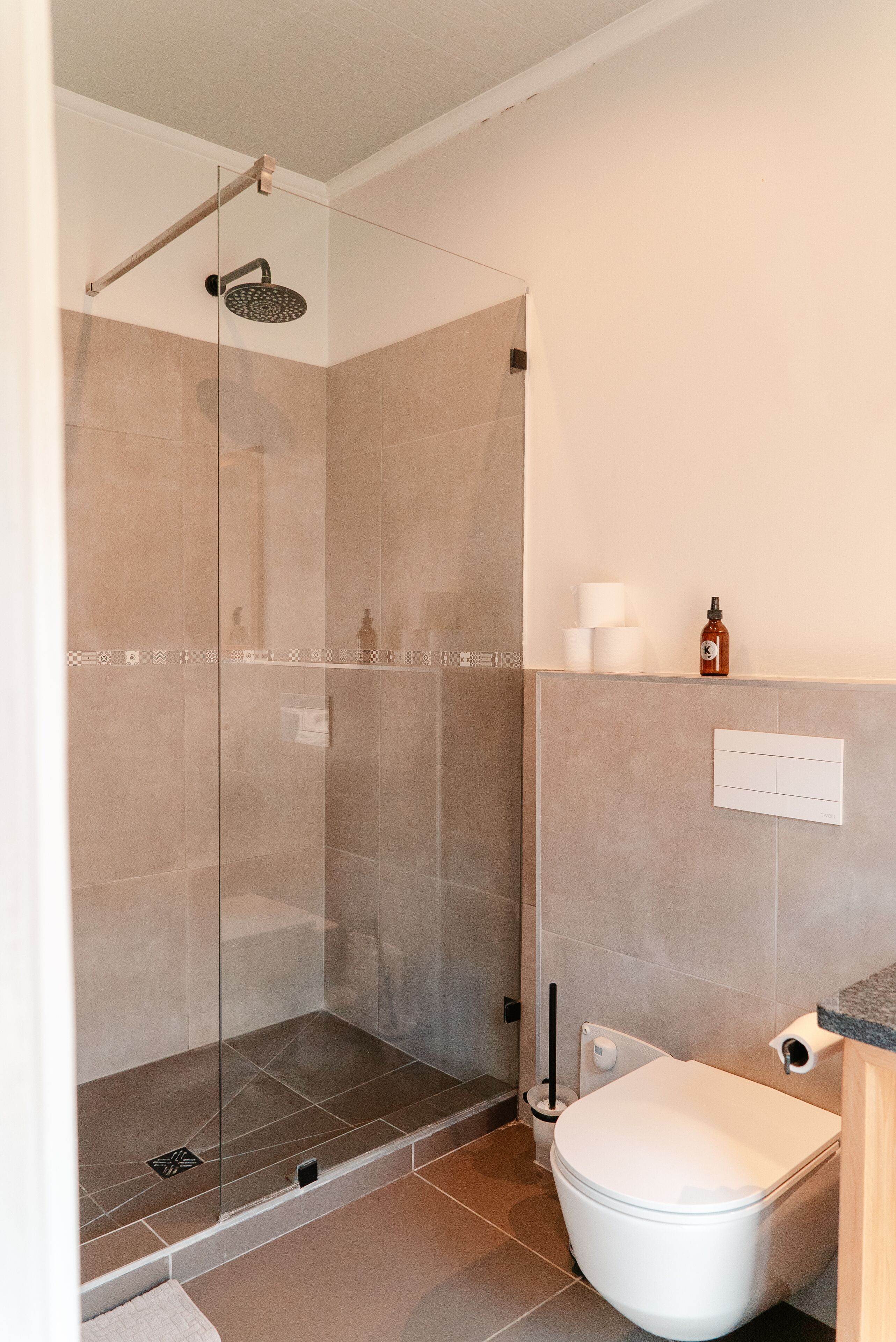A modern bathroom with a glass-enclosed shower, a toilet, and a shelf with toiletries.
