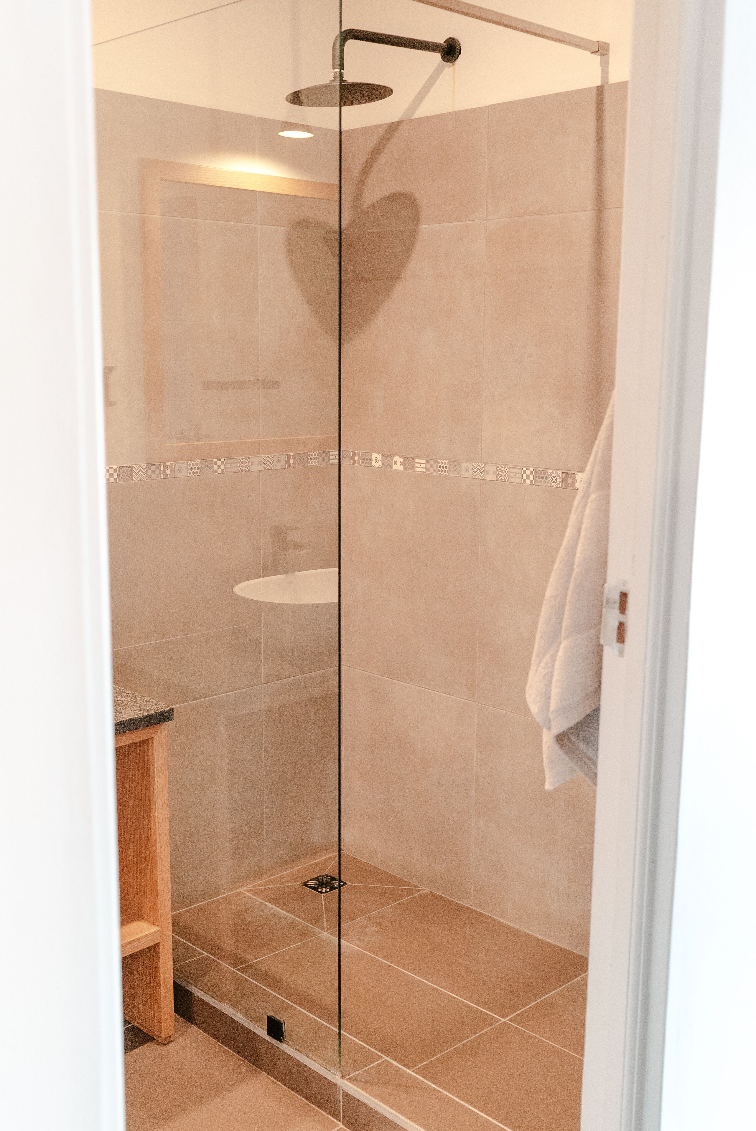 A glass-enclosed shower with beige tiles, a visible sink, and a towel hanging on the wall.
