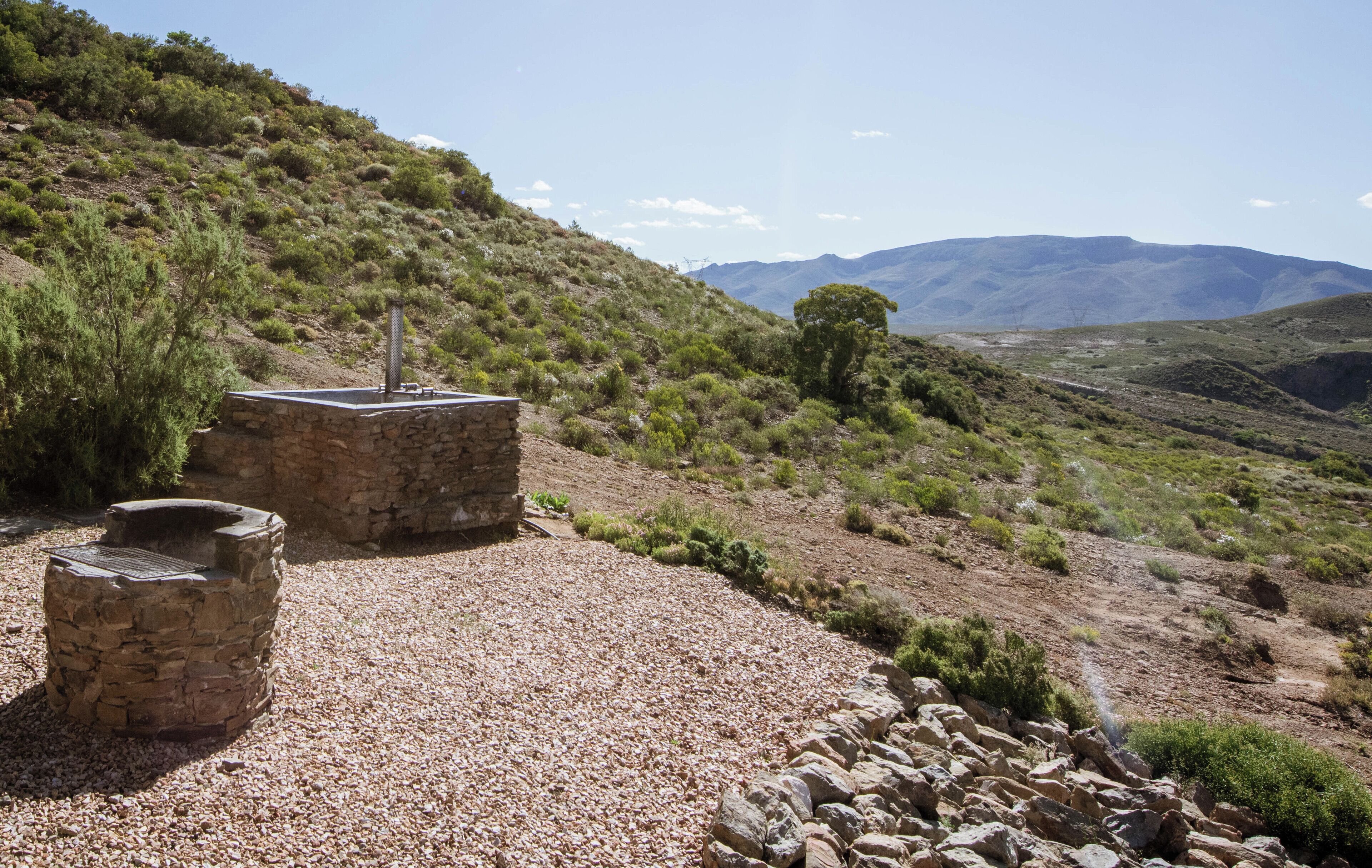 A stone structure with a chimney, surrounded by gravel and sparse vegetation on a hillside.