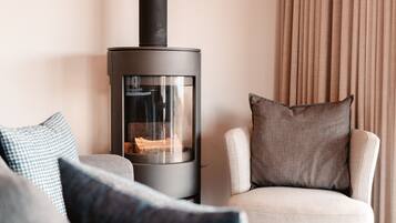A modern living room with a wood-burning stove, a beige armchair, and patterned cushions.
