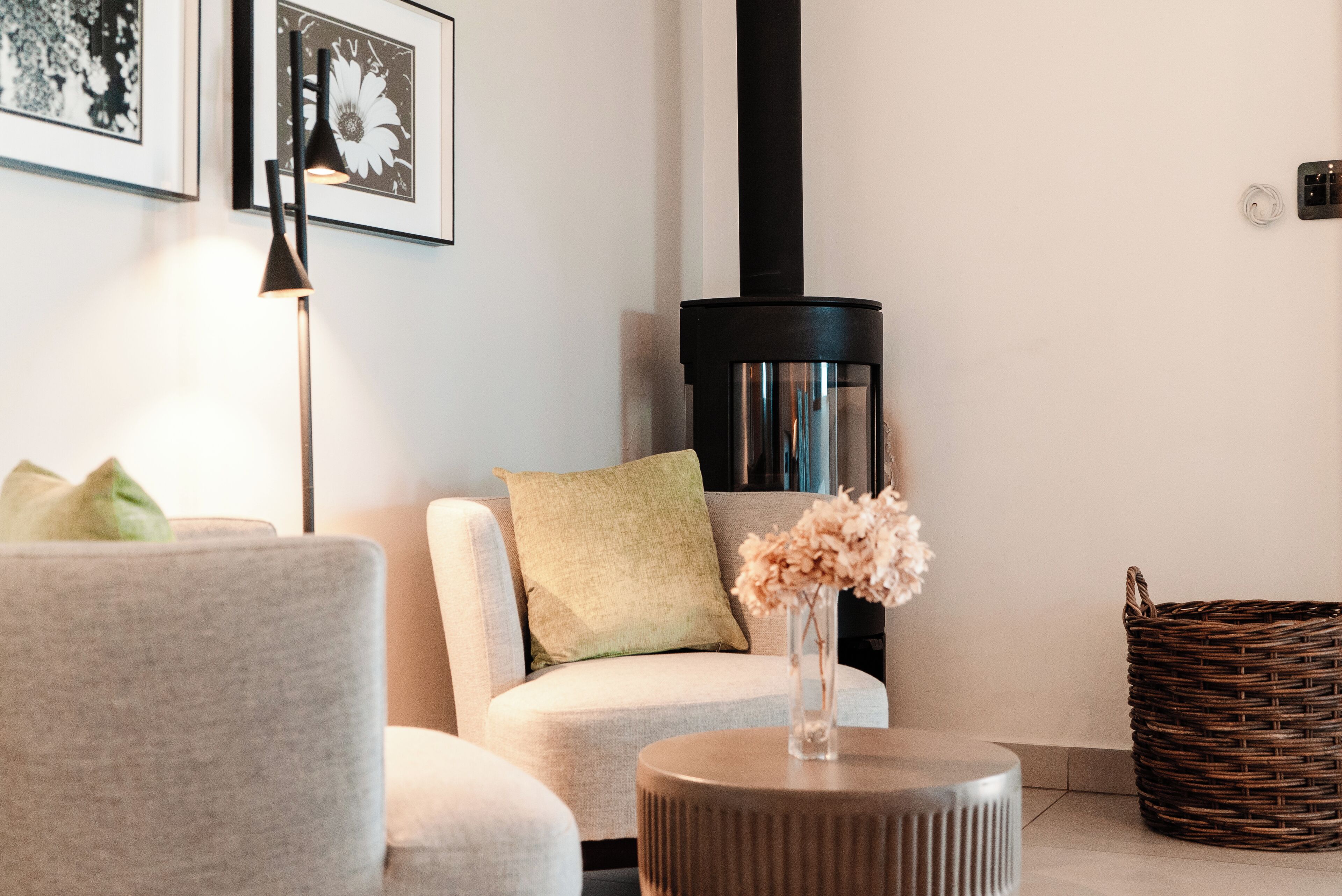 A modern living room with a sofa, a round coffee table, a vase with flowers, a floor lamp, a fireplace, and a wicker basket.