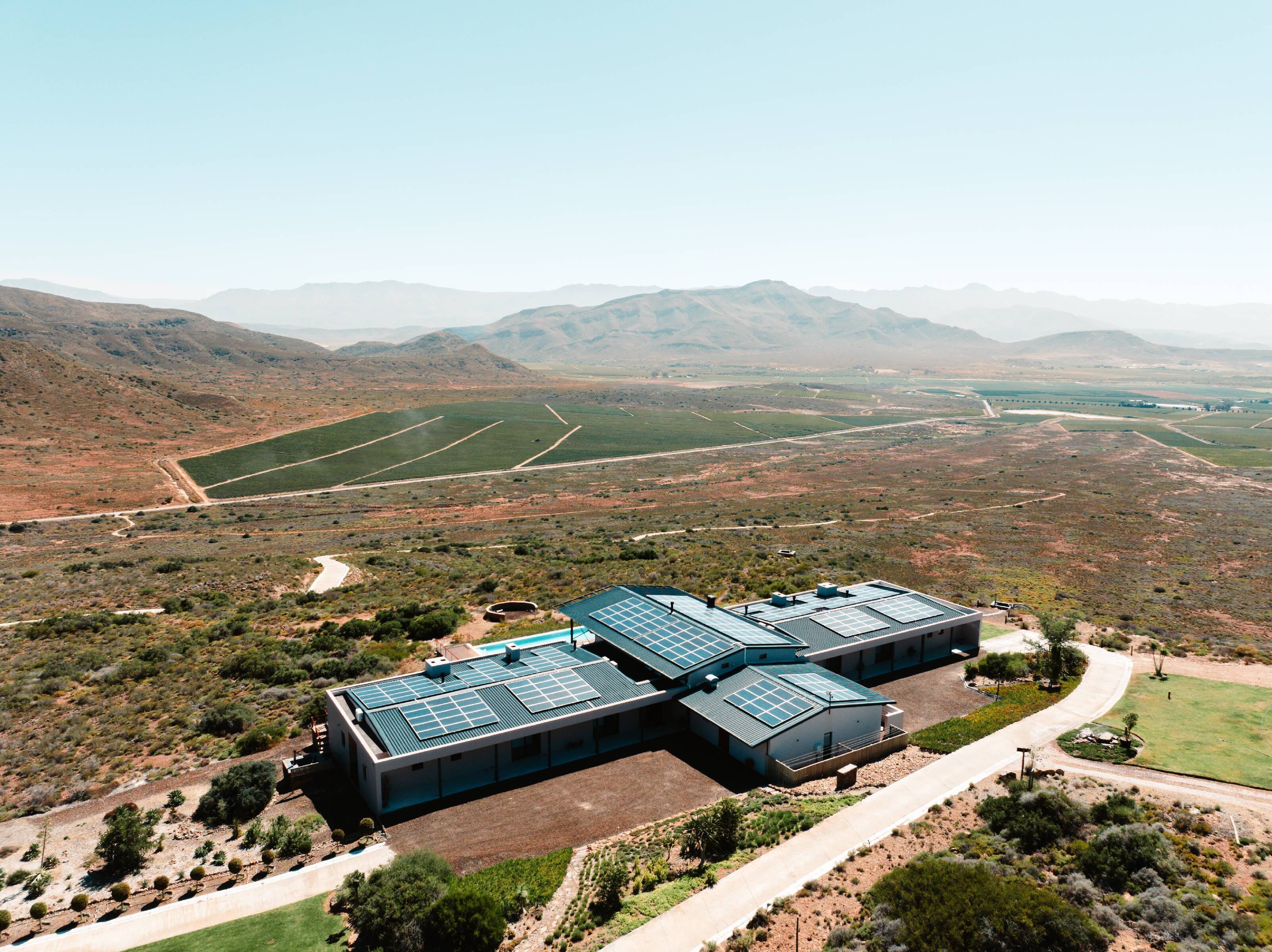 Un edificio moderno con varios paneles solares en el techo, rodeado por un paisaje desértico y montañas al lejano.