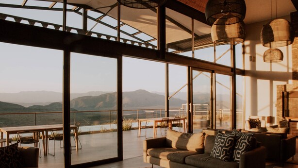 Amplia sala de estar con grandes ventanales con vistas a un paisaje montañoso.