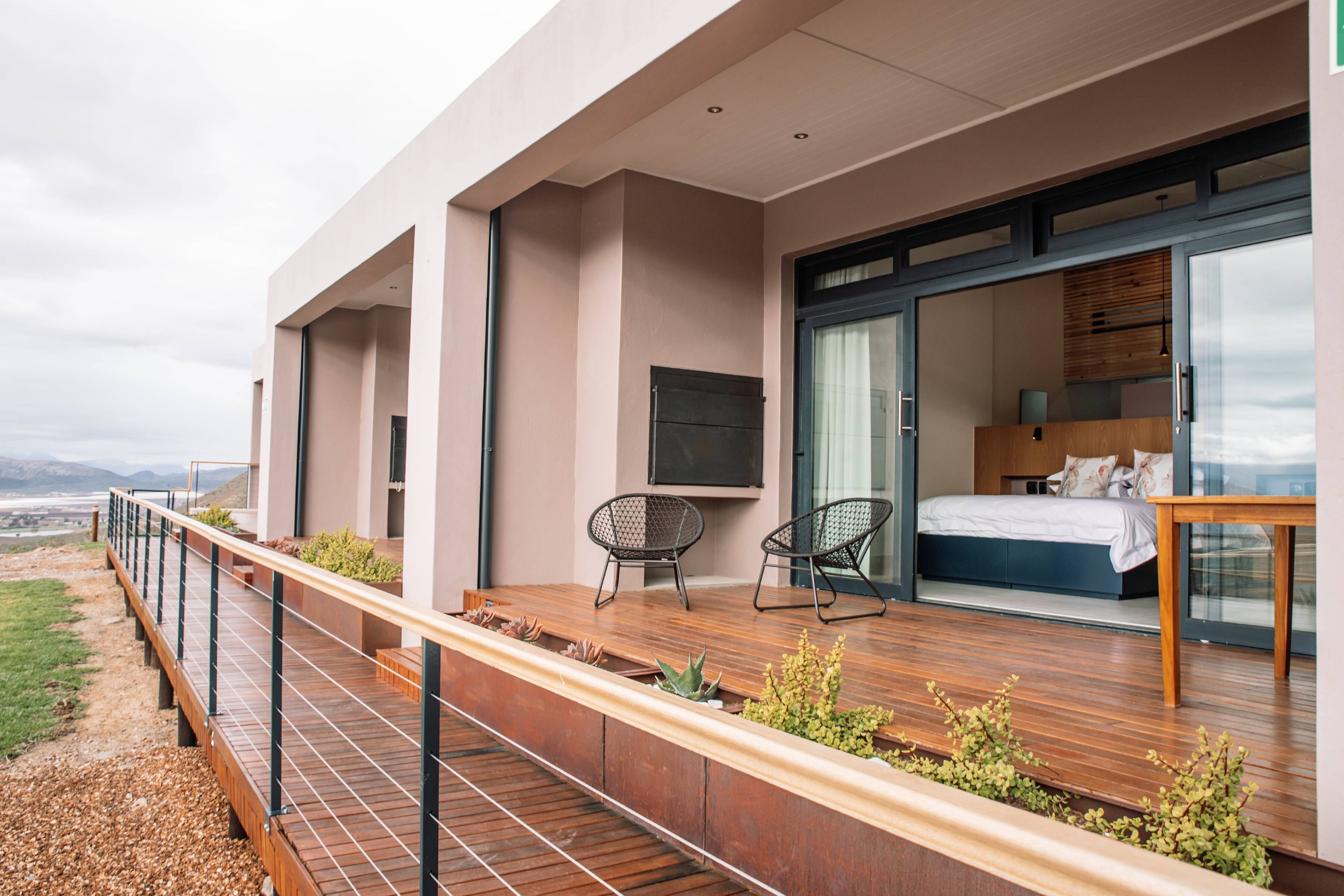 A modern bedroom with a large bed, a TV, and a balcony with seating and plants.