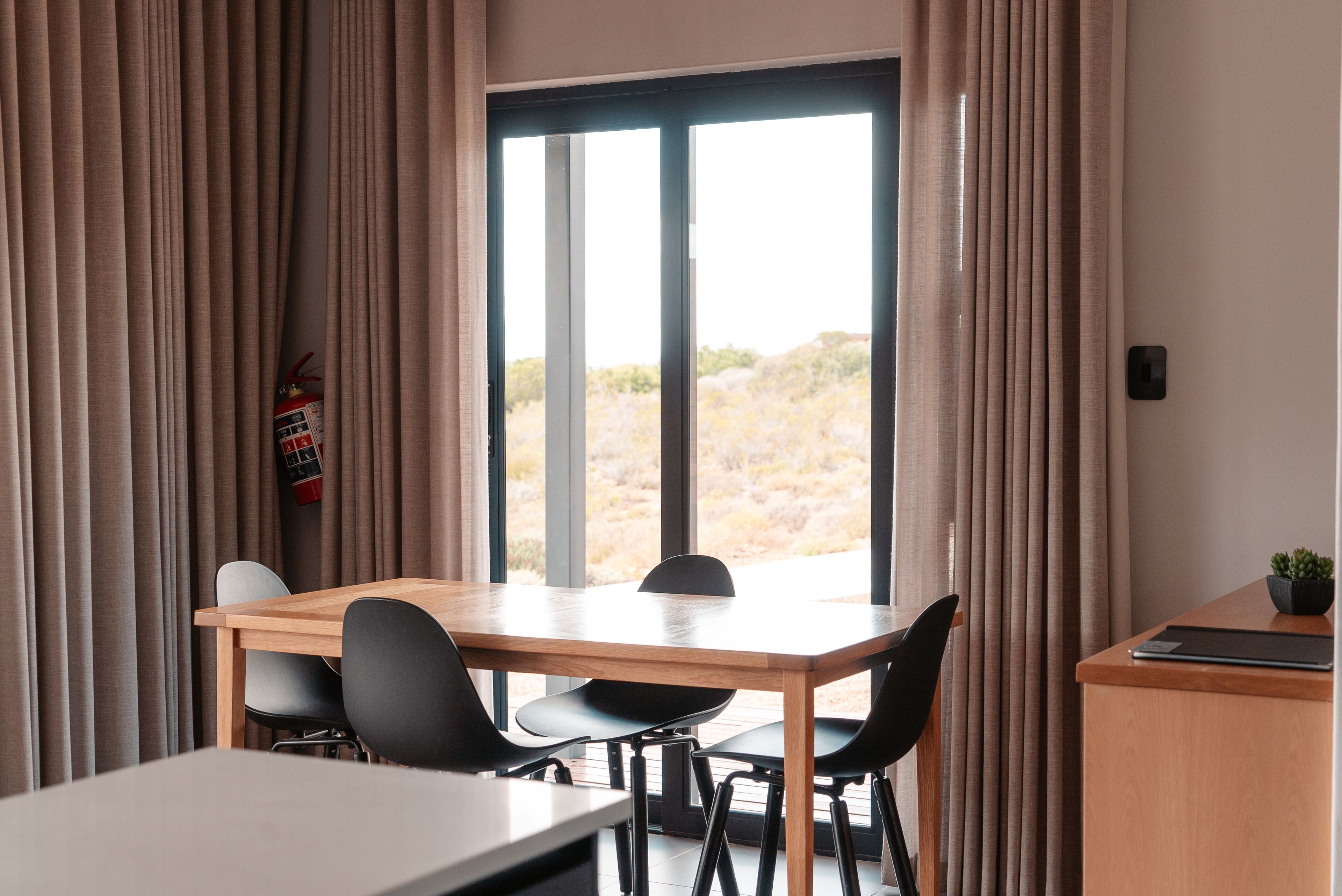 A room with a large window, a wooden table, and black chairs.